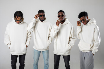 Group of African American guys in brown hoodies posing on a white background wearing sunglasses - Powered by Adobe