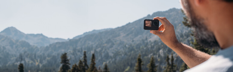 A male blogger shoots a video on an action camera in the mountains.