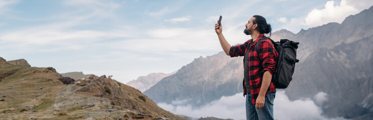 A male tourist with a large backpack and a phone in his hands.