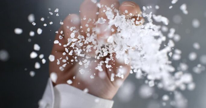 Super slow motion macro of stellar chef is putting heap of granulated rough crystal salt with flying grains while cooking in restaurant kitchen at 1000 fps.