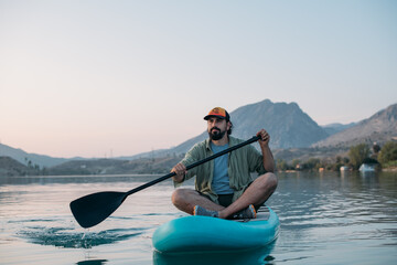 A man is surfing on a sup board on calm water at sunset.