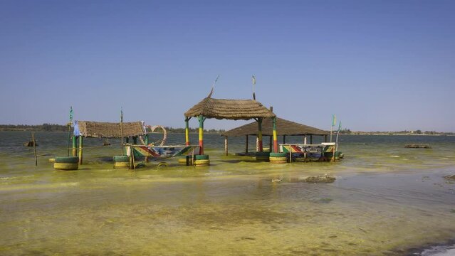 Pan right of thatched shelter on stilts on the shores of Lake Retba, Senegal. Lake Retba, also known as Lac Rose, is renowned for its vivid pink waters caused by Dunaliella salina algae. 4K UHD video.