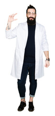 Doctor therapist man with long hair and bear wearing white coat smiling and confident gesturing with hand doing size sign with fingers while looking and the camera. Measure concept.