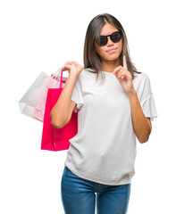 Young asian woman holding shopping bags on sales over isolated background serious face thinking about question, very confused idea