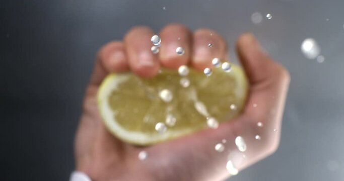 Super slow motion of professional bartender is squeezing fresh slice of lemon fruit while preparing an alcoholic cocktail with ice cubes to customers at the bar or disco club at 1000fps.
