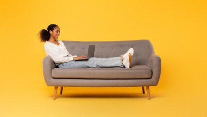 African American teen girl typing on laptop on sofa, studio