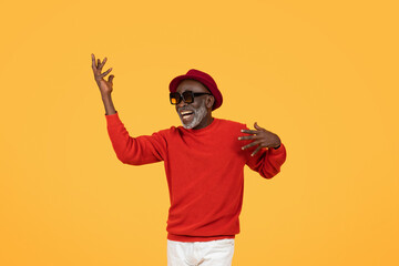 Exuberant senior man in a red sweater and hat, dancing with arms raised