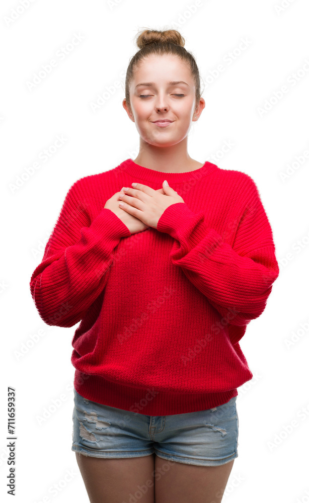 Sticker young blonde woman wearing bun and red sweater smiling with hands on chest with closed eyes and grat