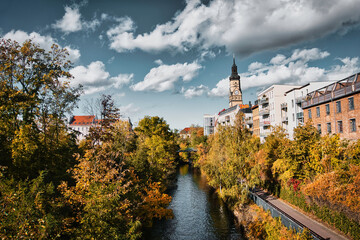River runs through the town,
Embraced by autumnal trees and a church that rises majestically in the...