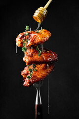 Grilled chicken wings baked in honey sauce on a fork. Honey stick with honey. On a black background.