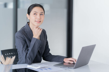 Sharing good business news. Attractive young businesswoman talking on the mobile phone and smiling while sitting at her working place in office and looking at laptop PC.