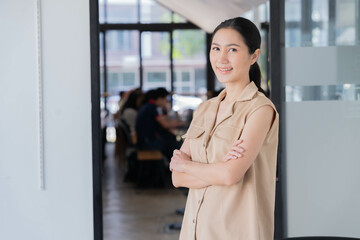 Portrait of young Asian businesswoman standing and smiling carrying her books. She looks confident,...