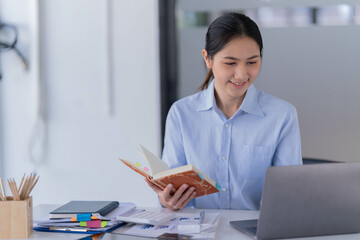 Sharing good business news. Attractive young businesswoman talking on the mobile phone and smiling while sitting at her working place in office and looking at laptop PC.