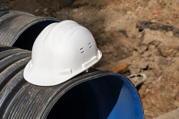 Close-up of a white plastic safety helmet on a black corrugated pipe.