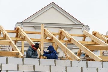 Two carpenters are working on a wooden roof structure at a construction site. Industrial roofing...