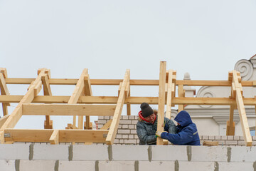 Two carpenters are working on a wooden roof structure at a construction site. Industrial roofing system with wooden beams, ceilings and tiles. Roofing works.