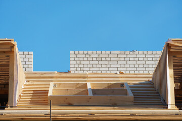 A new wooden roof structure lining a house in the city. Industrial roofing system with wooden beams, ceilings and tiles. Roofing works.