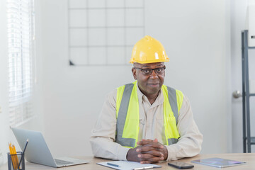 Professional of man architect industrial engineer Standing in the office, foreman in helmet using laptop working with new construction project architectural plan.