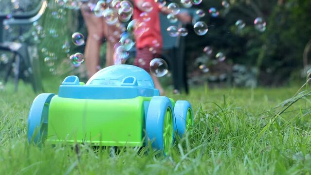 A plastic toy blows soap bubbles in the garden, a mother and son are playing on a blurred background