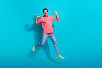 Fototapeta na wymiar Full length photo of impressed funky man wear pink t-shirt jumping high pointing thumbs herself isolated blue color background