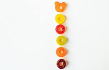 A vertical arrangement of colorful gummy candies on a white background. One candy is shaped like a bear s head.