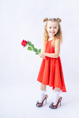 a little happy child girl in a red dress and in her mother's big shoes with a rose in her hand on a white isolated background laughs and smiles, the concept of Valentine's day, a place for text
