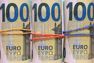 Banknotes of one hundred Euros in rolls, fastened with an elastic band, close-up.