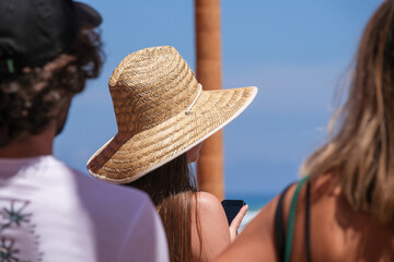 Young people and woman with sun hat watching sport competition on the beach against the ocean