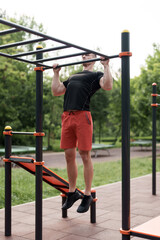 A man in a black t-shirt does pull-ups at an outdoor fitness park, demonstrating his commitment to physical health