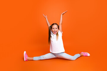 Full body portrait of overjoyed sporty schoolchild raise arms split legs isolated on orange color background