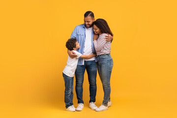 Little black boy embracing his parents while they standing on yellow background