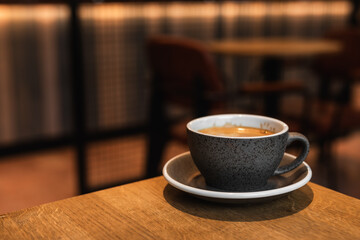 Cup of black coffee on the edge of a wooden table in a cafe coffee-shop with copy space