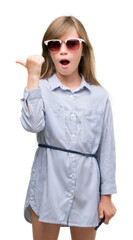 Young blonde toddler wearing blue shirt pointing with hand and finger up with happy face smiling