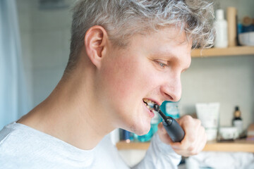 Close up portrait of Young Man is using electric ultrasound toothbrush. Male brushing teeth. Daily dental hygiene and oral health. Morning routine, young man cleaning his teeth. Selective focus