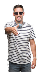 Handsome young man wearing headphones smiling friendly offering handshake as greeting and welcoming. Successful business.