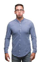 Handsome young elegant man wearing glasses puffing cheeks with funny face. Mouth inflated with air,...