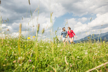glückliches Paar rennt durch Wiese in den Bergen, Österreich