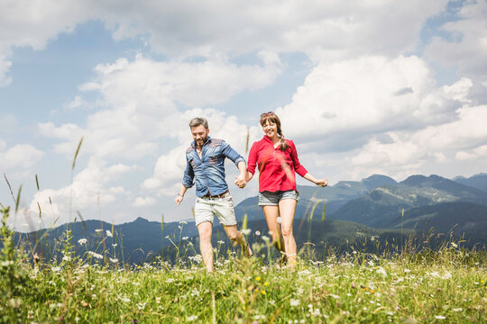 glückliches Paar rennt durch Wiese in den Bergen, Österreich