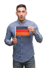 Handsome young man holding a flag of Germany scared in shock with a surprise face, afraid and excited with fear expression