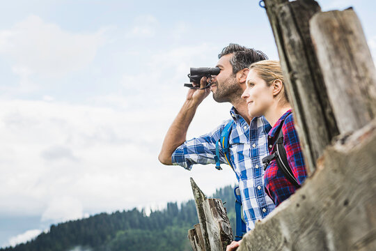 gl&uuml;ckliches Paar in Karohemden  mit Fernglas an einer Alm in den Bergen, &Ouml;sterreich