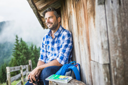 male hiker relaxing on pile of wood at a cabin enjoying the mountains