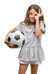 Brunette hispanic girl holding soccer football ball with happy face smiling doing ok sign with hand on eye looking through fingers