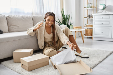 attractive jolly african american woman talking by phone while sitting on floor next to her parcel