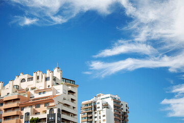 The upper floors of high-rise buildings are set against a blue sky with white clouds during the day. Copy space.
