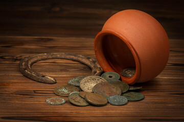St Patricks day concept with pot with scattered old coins and horseshoe on vintage wooden background, close up