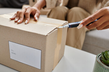 cropped view of young african american woman opening box with stationery knife next to plan on table