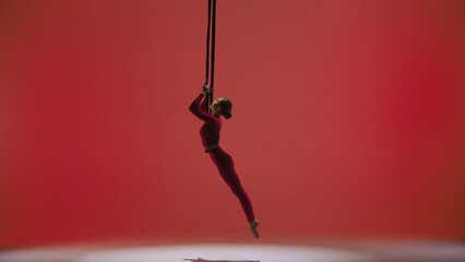 Female gymnast isolated on red studio background. Girl aerial dancer in bodysuit on acrobatic...