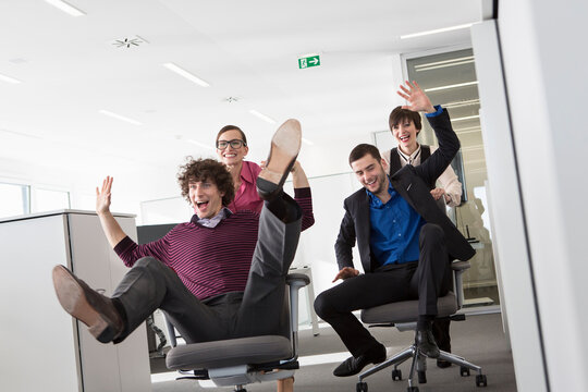 Kollegen machen Bürostuhlrennen im Büro, München, Deutschland