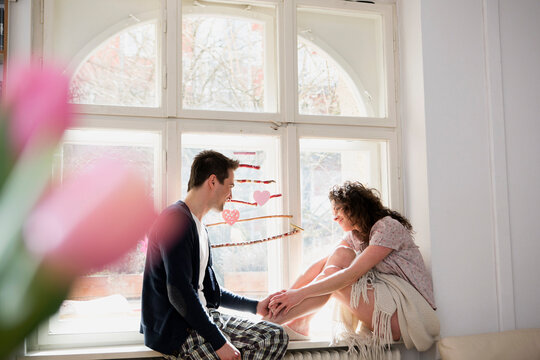 cute couple in love sitting on the windwo sill in pajamas and dreaming