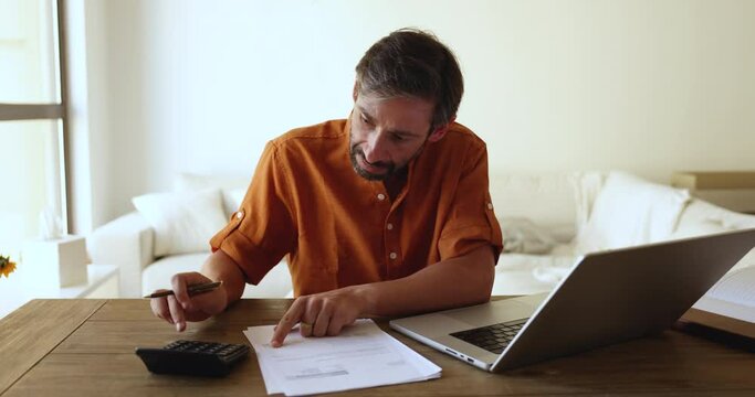 Portuguese middle-aged man doing accountancy work at home, sit at desk calculates expenses, control incomes on calculator, pay household bills, taxes use laptop and e-banking app. Finances management